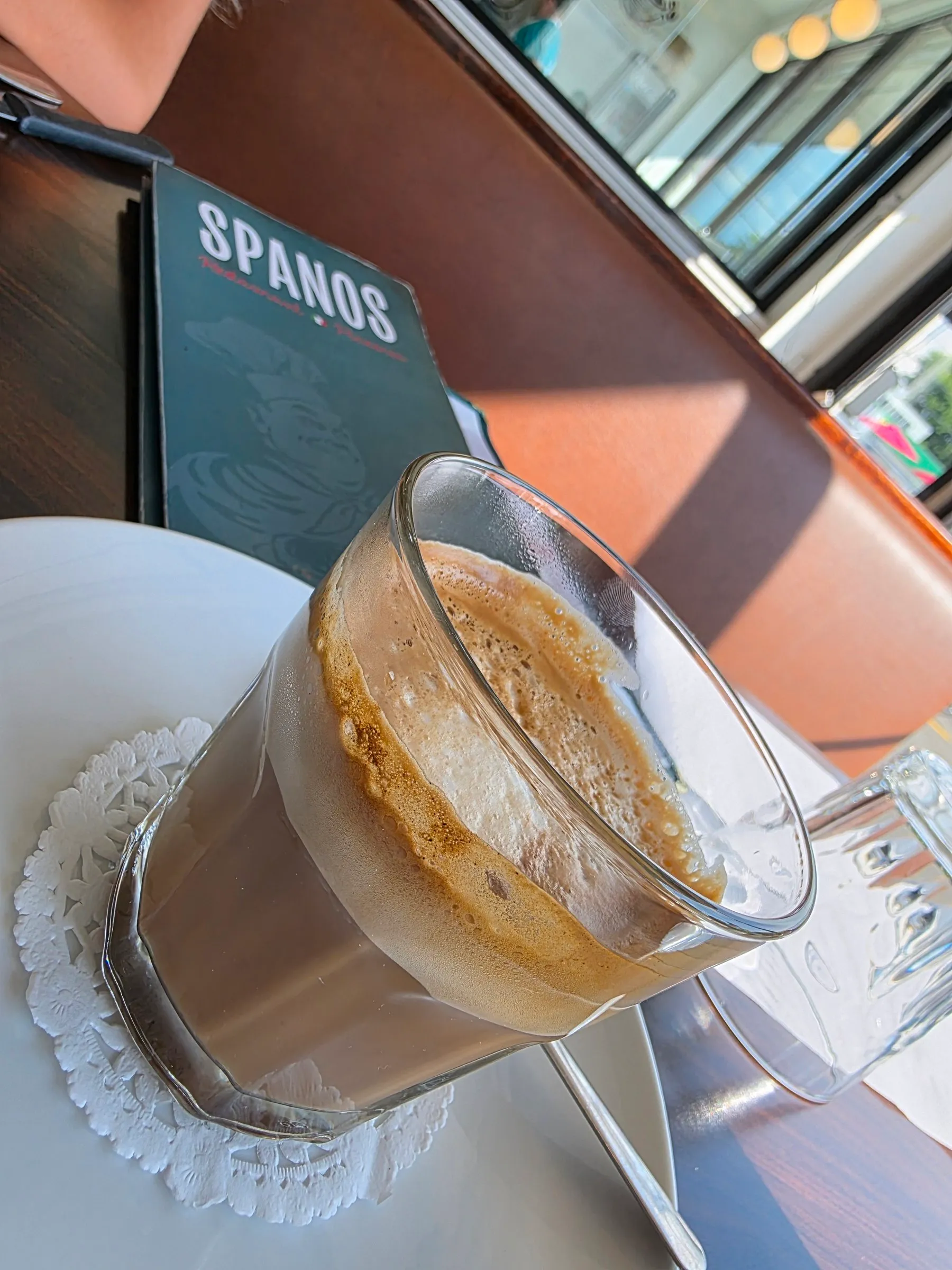 Café au lait dans un verre, avec le menu Spanos sur la table