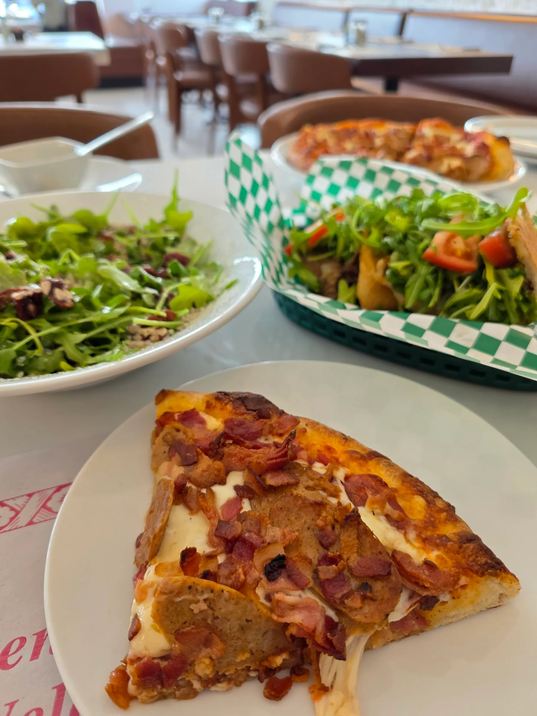 Pointe de pizza au bacon, avec salade et sandwichs en arrière-plan