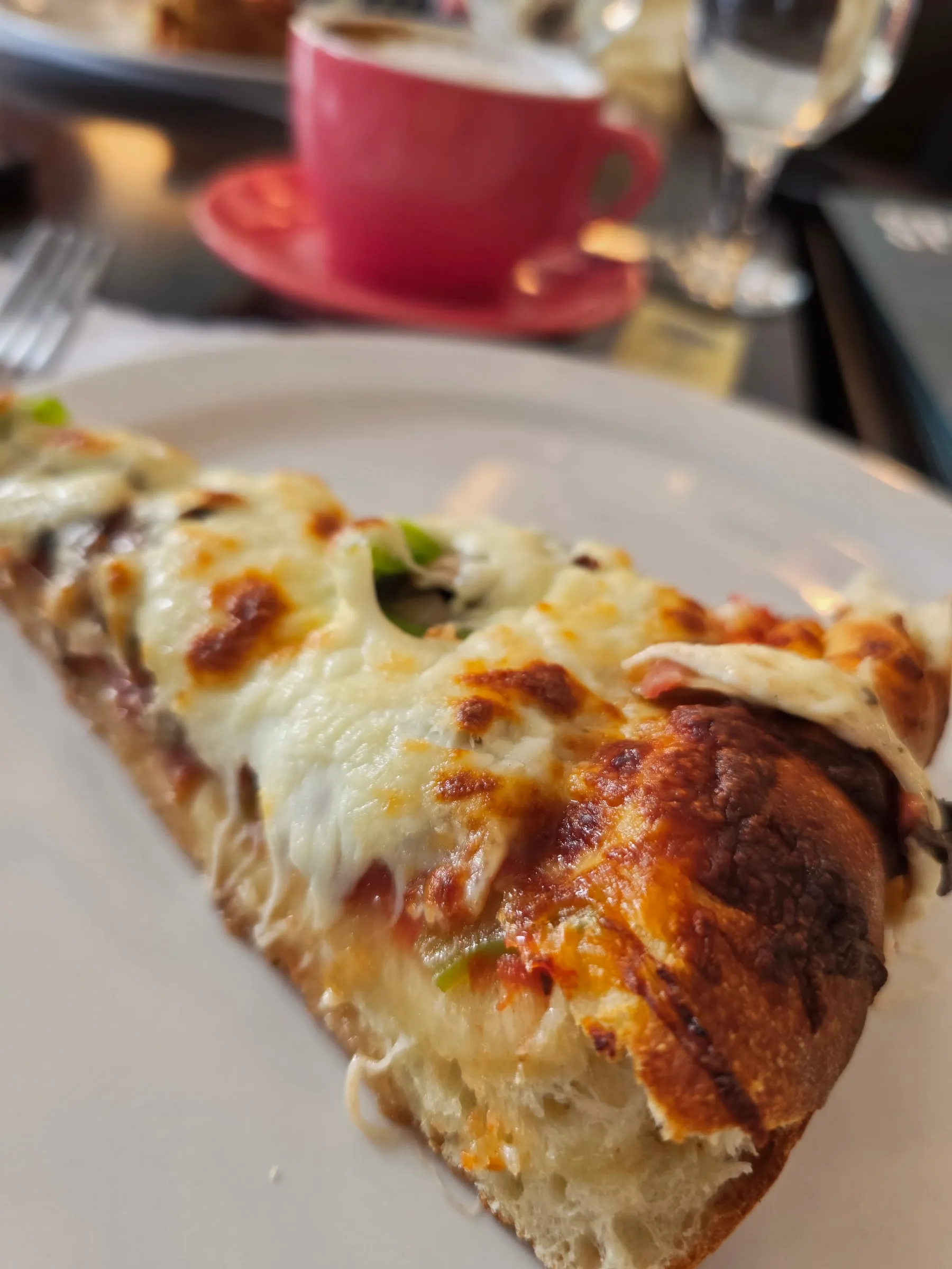 Pointe de pizza gratinée servie avec un café