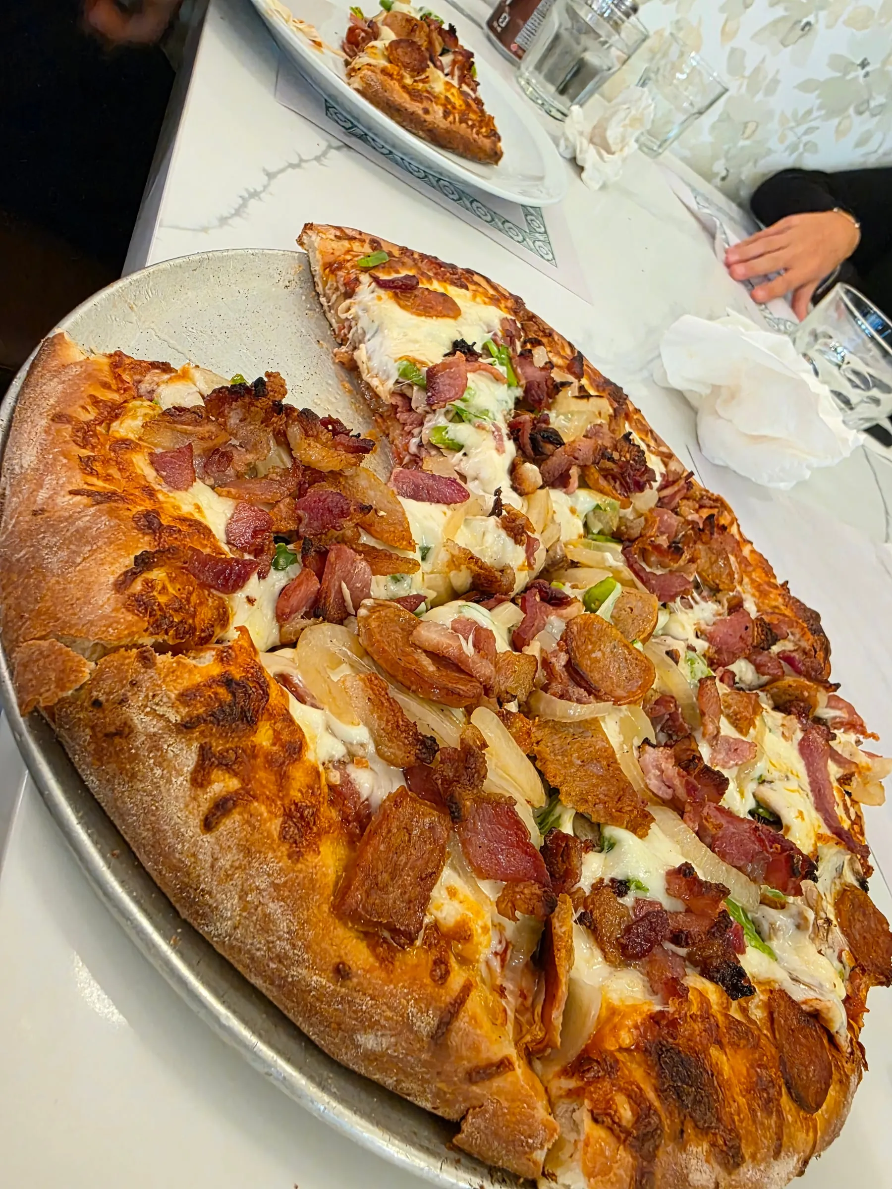 Pizza bien garnie de bacon, saucisses et oignons chez Spanos