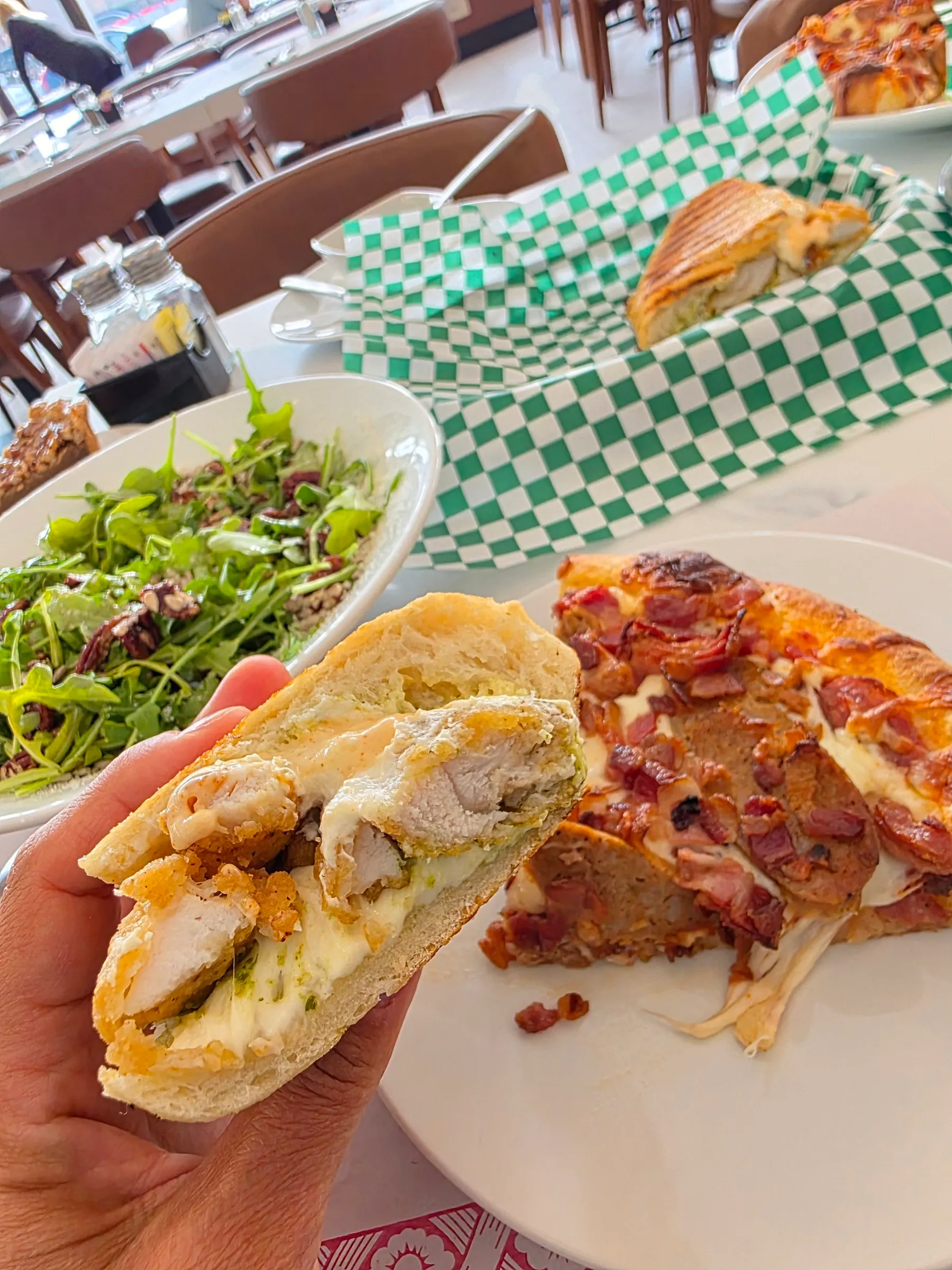 Sandwich au poulet tenu à la main, avec une pointe de pizza derrière